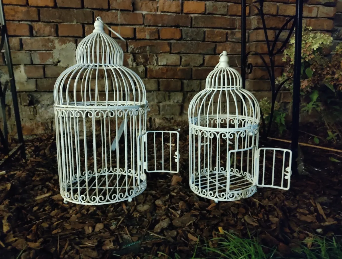 Two white birdcages standing open against a brick wall